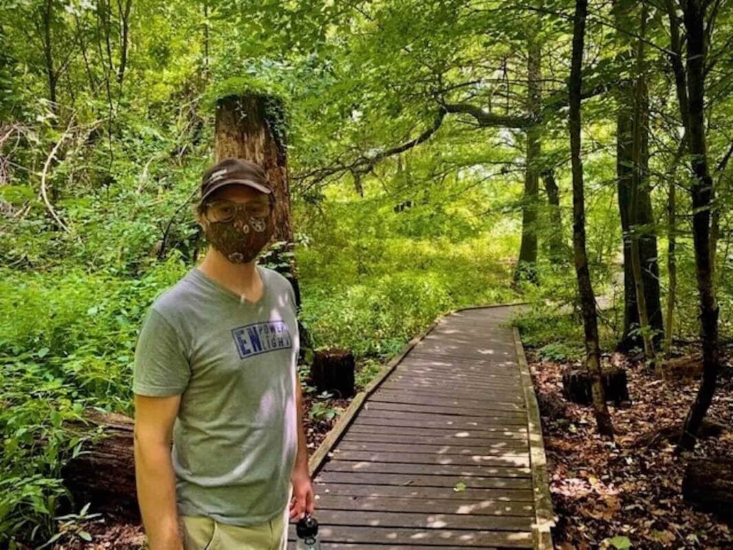 man wearing mask outdoors on boardwalk trail in the woods