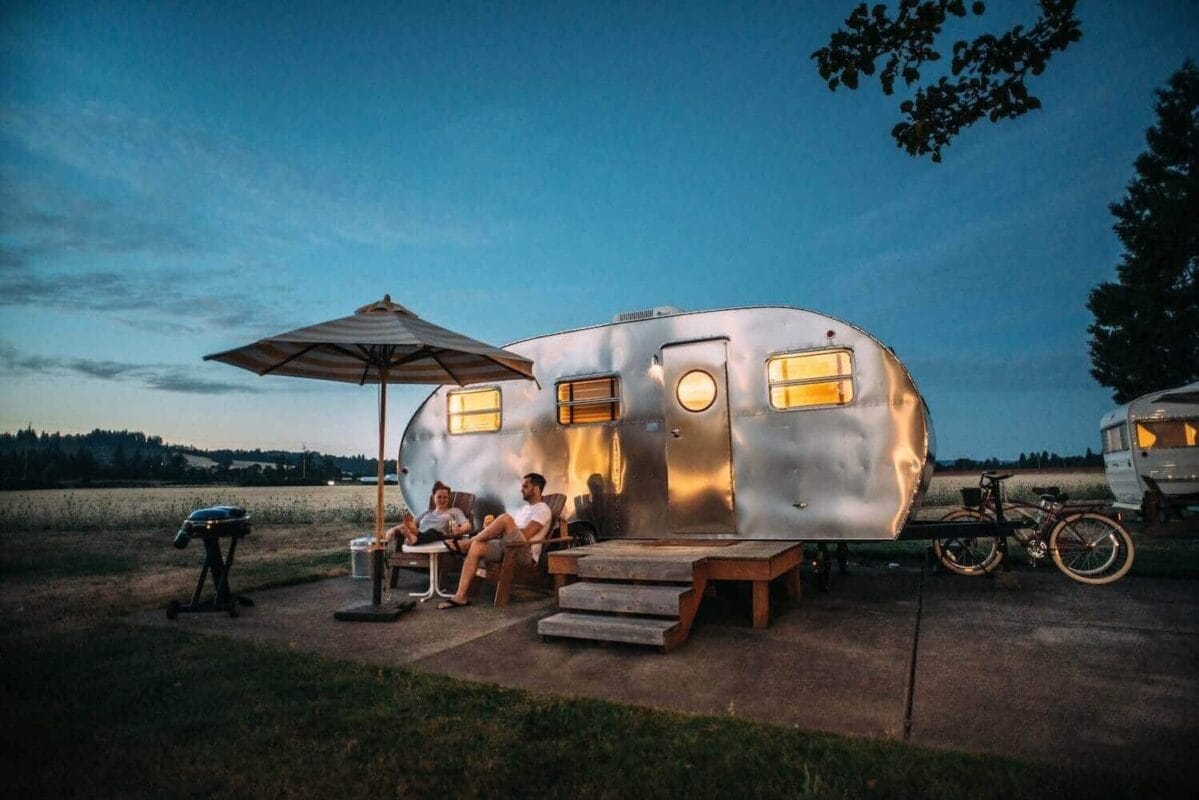 metal rv camper trailer parked at campsite with umbrella and seating set up in front