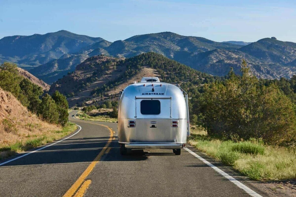 the back of an airstream trailer driving down a scenic road toward mountains