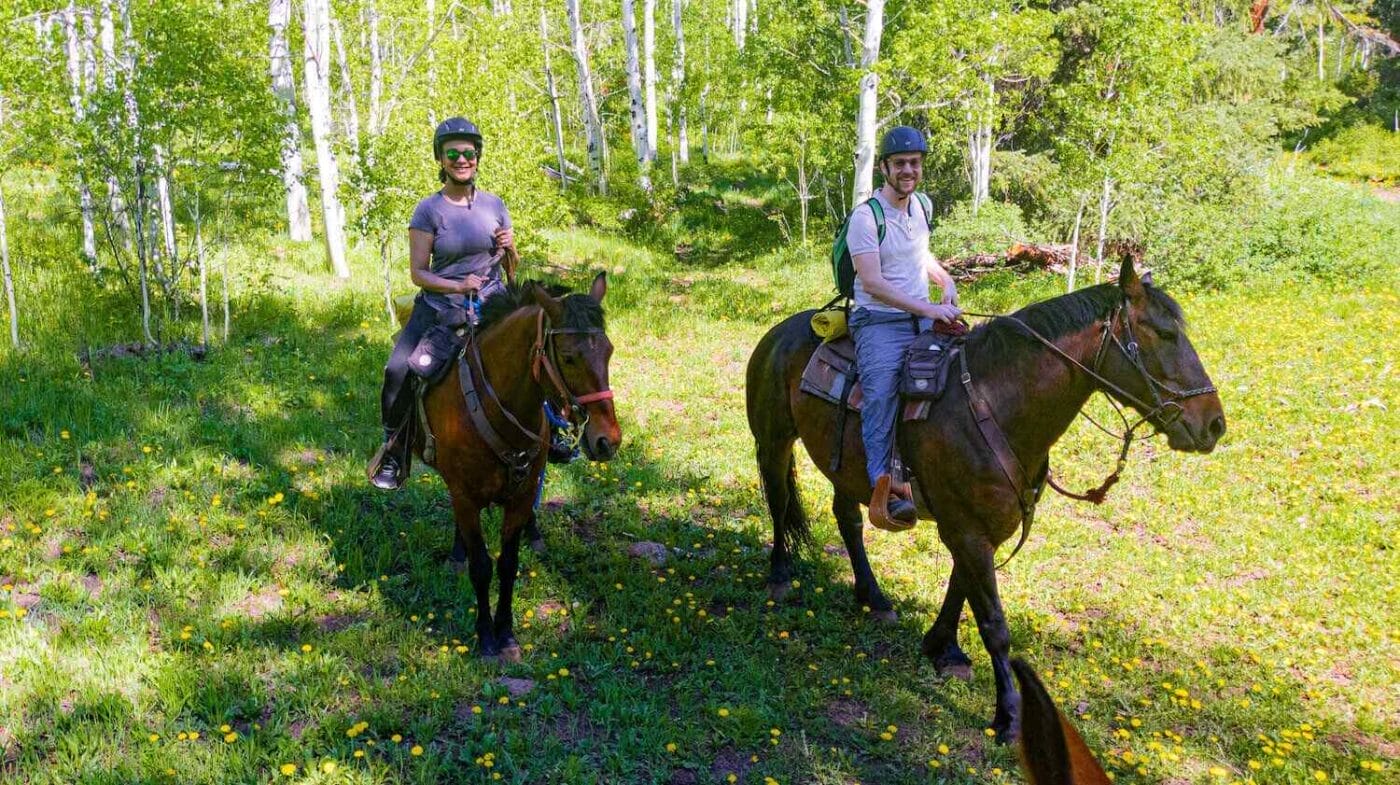 travel couple on horses wearing helmets in the forest