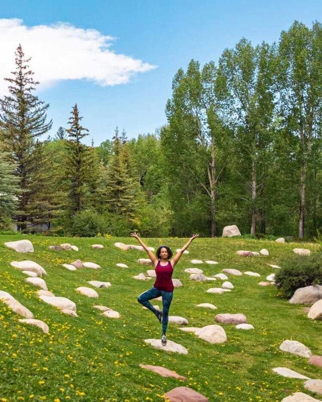 woman doing yoga tree pose in rock garden surrounded by trees in Aspen