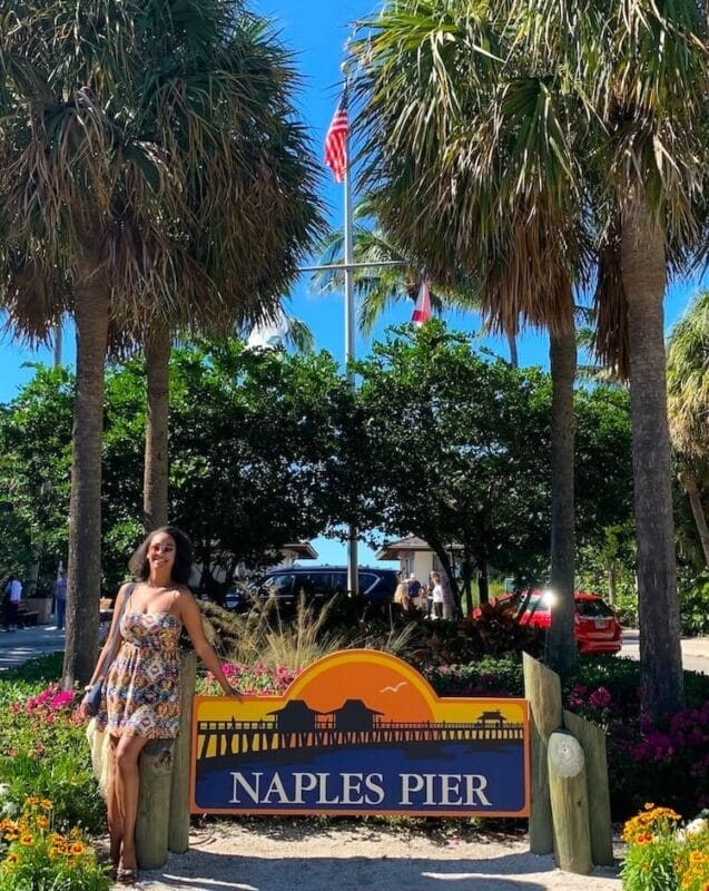 standing next to a Naples Pier sign with palm trees