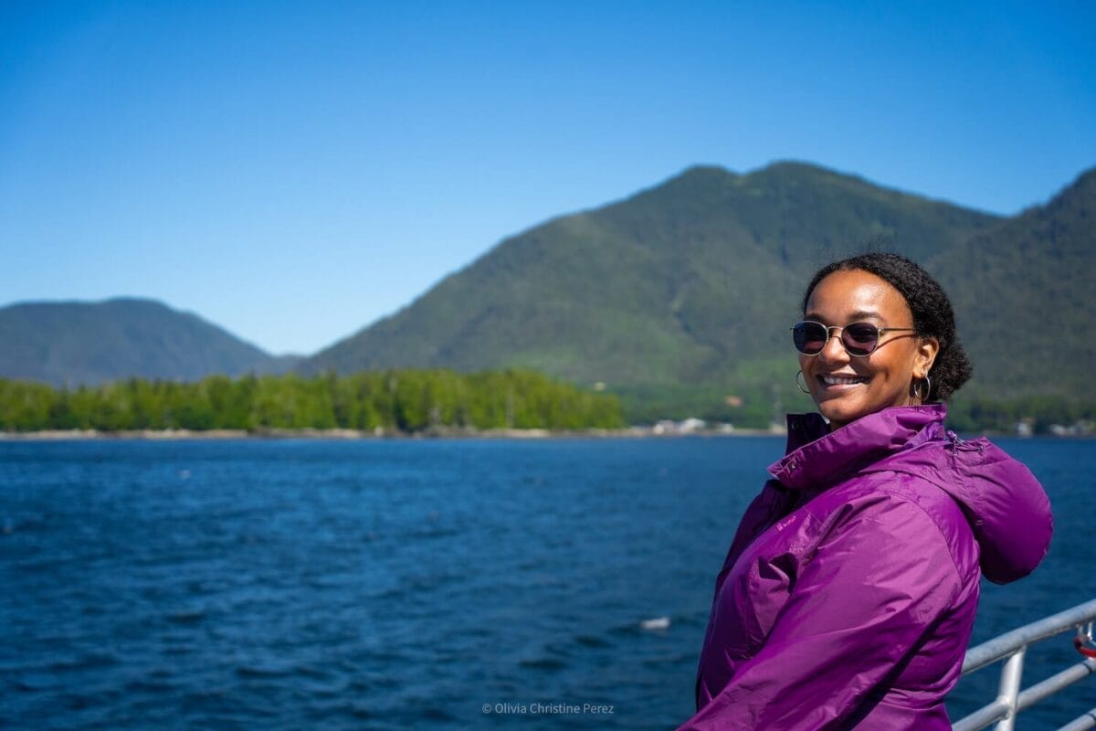 black female traveler with view of mountains and blue sea on a small boat tour