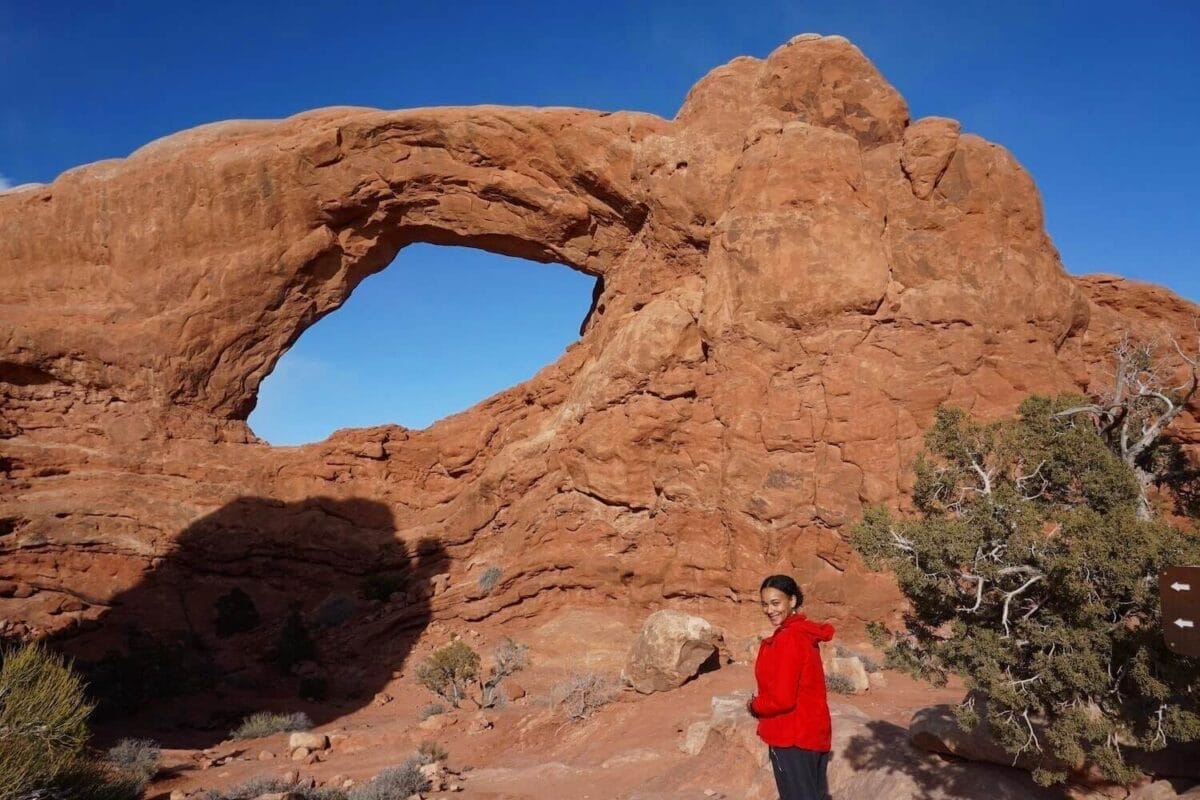 Small red rock window in Arches national park with black female hiker