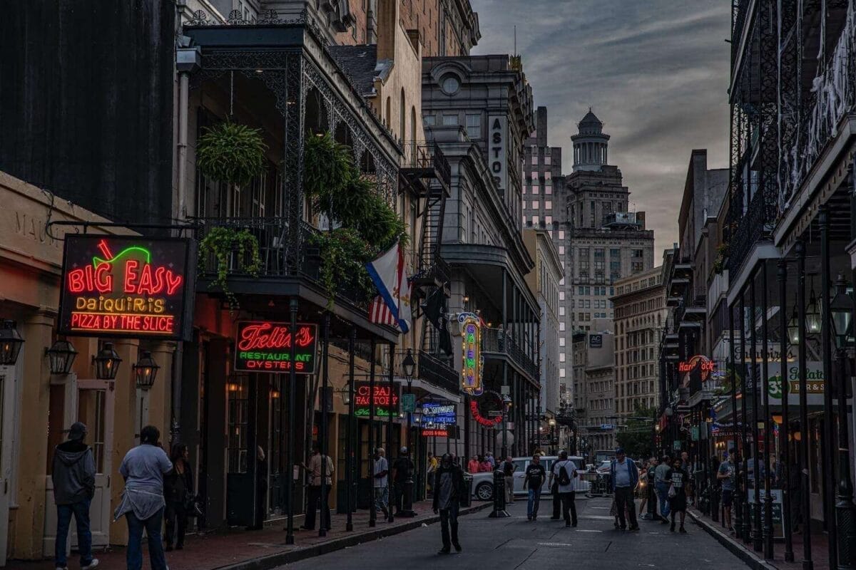 NOLA french quarter at sunset with pedestrians walking and store and restaurant signage lit up