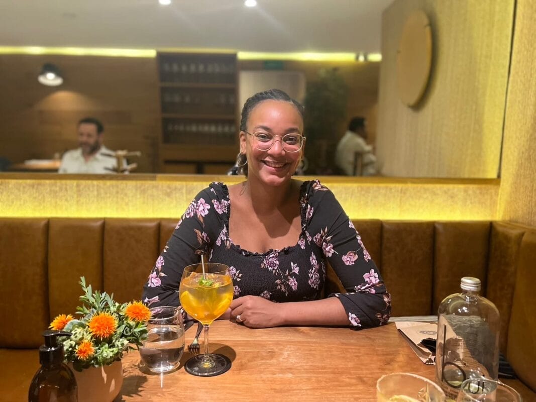 Olivia sitting at a table with a cocktail and flowers