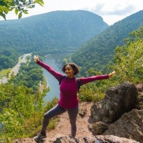 black female hiker celebrating at high viewpoint on hike, overlooking the delaware river