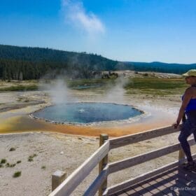 olivia standing along a boardwalk overlooking a colorful hot spring